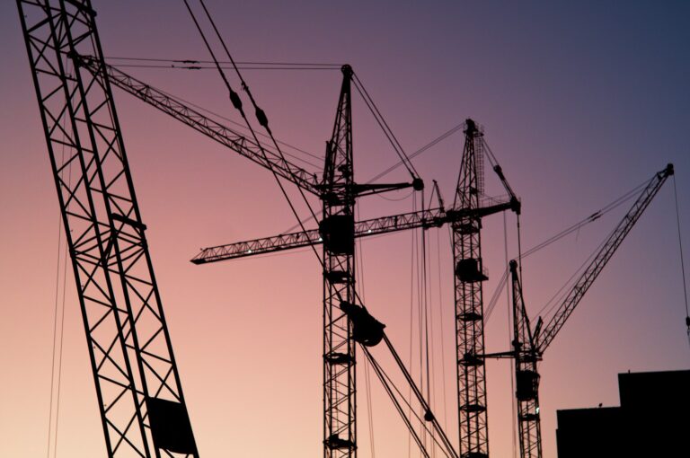 Several tower cranes rising over a city construction site